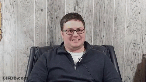 Smiling Man In Glasses Sitting In Chair GIF