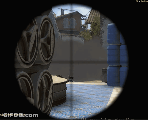 Sniper Scope Showing Stack Of Barrels And Building In Distance GIF
