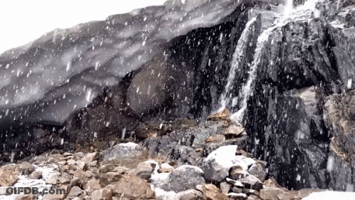 Snow Is Falling On A Rocky Hillside With A Waterfall GIF