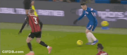 Soccer Player In Blue Jersey Kicking Ball While Red Shirt Watches GIF