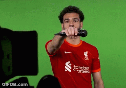 Soccer Player In Red Shirt Holding Microphone Pointing At Camera GIF