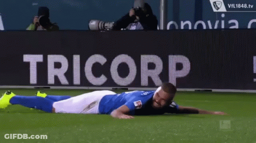 Soccer Player Laying On Field In Front Of Tricorp Banner GIF