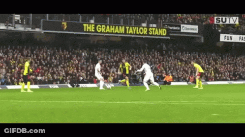 Soccer Players On A Field With A Sign That Says The Graham Taylor Stand In The Background GIF
