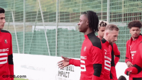 Soccer Players Standing In Front Of Football Impact Fence GIF