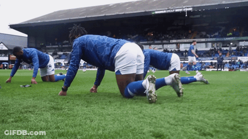 Soccer Players Stretching On The Field In Front Of A Sign That Says Magnus Group West End GIF