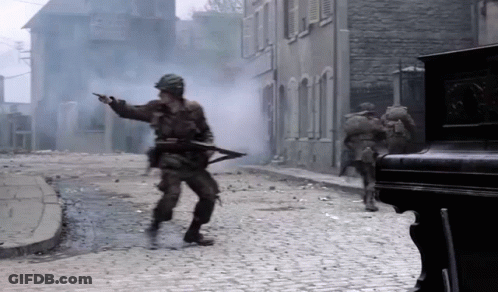 Soldiers Are Walking Down A Cobblestone Street With Smoke Coming From The Buildings GIF