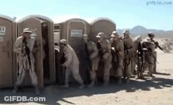 Soldiers Standing In Front Of Portable Toilets In Desert GIF