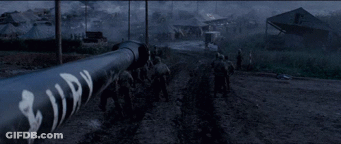 Soldiers Walking Down Dirt Road Past Building Saying A GIF