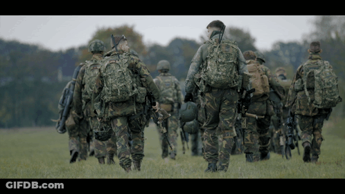 Soldiers Walking In Field, One With Helmet GIF