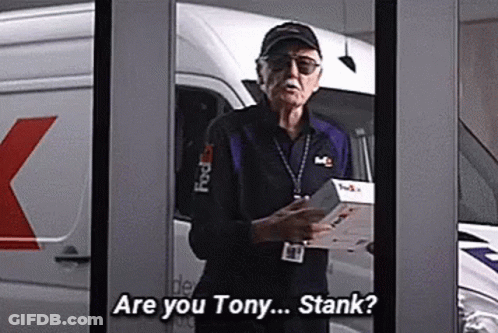 Stan Lee Is Standing In Front Of A Fedex Van Holding A Box And Talking To Someone . GIF