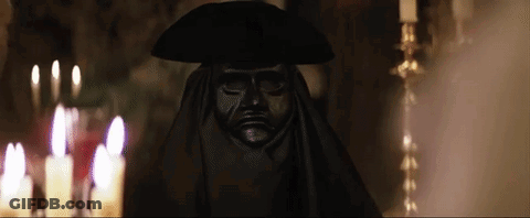 Statue Of Man In Black Mask And Hat In Front Of Candles GIF