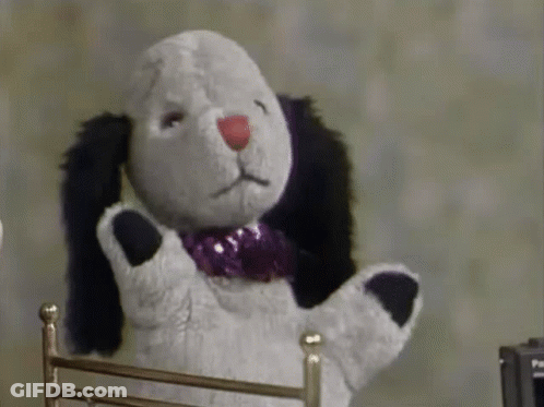 Stuffed Animal With Purple Bow Tie Sitting In Chair GIF
