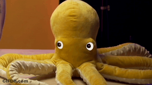 Stuffed Octopus With Big Eyes On Wooden Table GIF