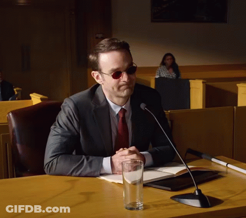 Suited Man At Desk With Microphone And Water GIF