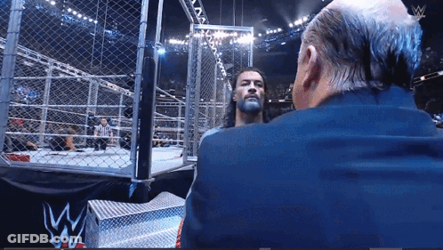 Suited Man Talking In Wrestling Ring W Logo GIF