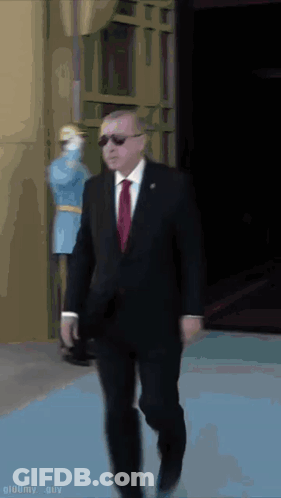 Suited Man Walking On Blue Carpet, Masked Man Behind GIF