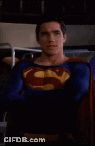Superman Costume Man Standing With Arms Crossed In Dark Room GIF