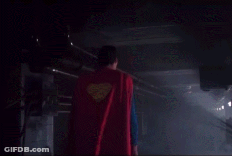 Superman Is Walking Through A Dark Room With A Red Cape On . GIF