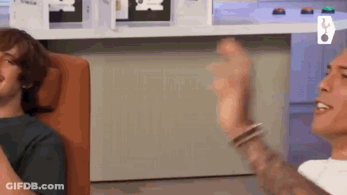 Tattooed Man Sitting While Another Throws Ball GIF
