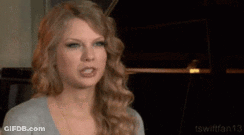 Taylor Swift Is Making A Funny Face While Wearing A Gray Shirt . GIF