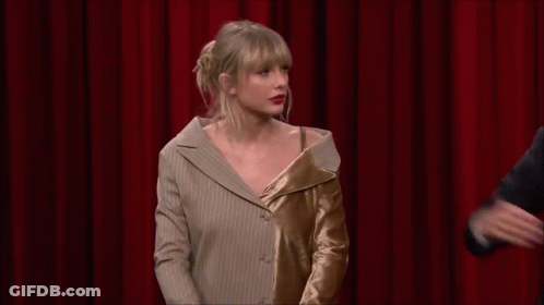 Taylor Swift Is Standing In Front Of A Red Curtain With A Man In A Suit . GIF