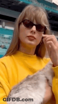 Taylor Swift Wearing Sunglasses And Yellow Sweater Holding Cat GIF
