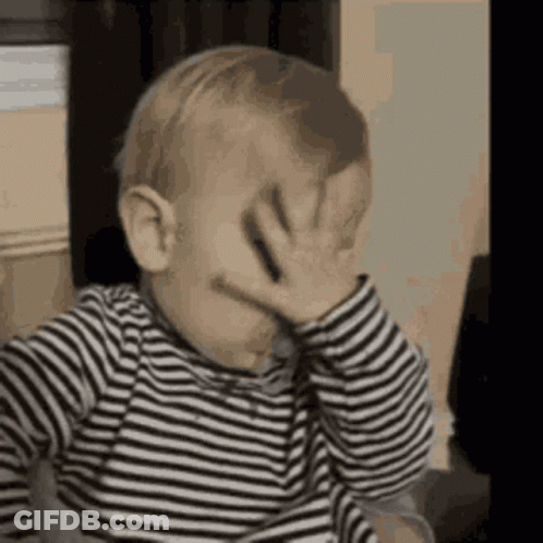 The Baby Is Wearing A Striped Shirt And Covering His Face With His Hand . GIF