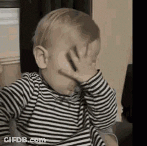 The Baby Is Wearing A Striped Shirt And Covering His Face With His Hand . GIF
