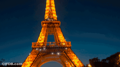 The Eiffel Tower Is Lit Up At Night Against A Dark Blue Sky GIF