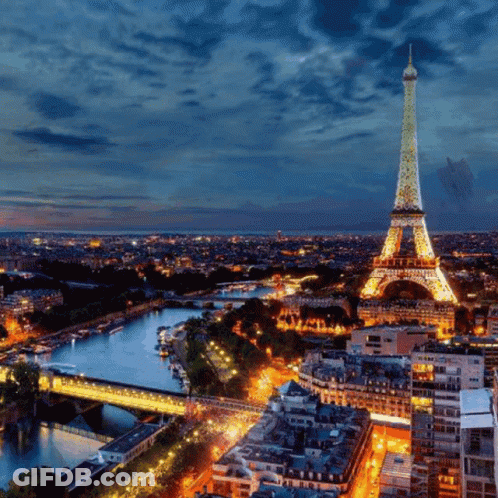 The Eiffel Tower Is Lit Up At Night With A Blue Sky In The Background GIF