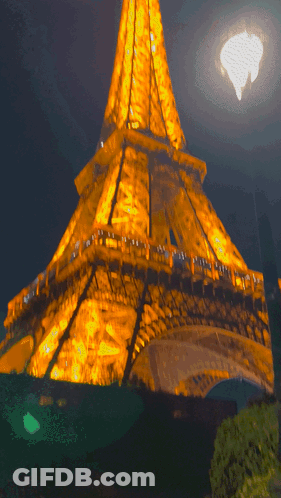 The Eiffel Tower Is Lit Up At Night With A Full Moon GIF