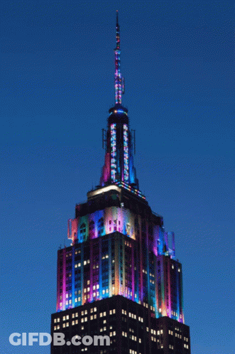 The Empire State Building Is Lit Up With Colorful Lights At Night GIF