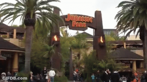 The Entrance To Jurassic Park Is Shown With Palm Trees In The Background GIF