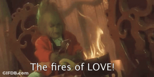 The Grinch Is Sitting In Front Of A Fireplace With The Words `` The Fires Of Love '' Written On The Screen . GIF