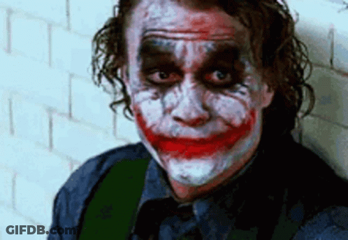 The Joker Is Leaning Against A Wall With His Face Painted And Making A Funny Face . GIF