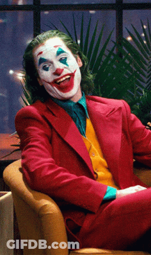 The Joker Is Sitting In A Chair And Smiling GIF
