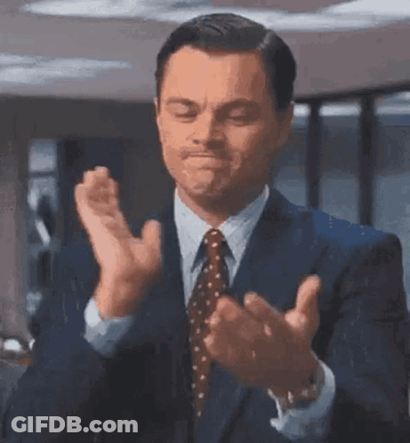 The Man Is Wearing A Suit And Tie And Clapping His Hands . GIF