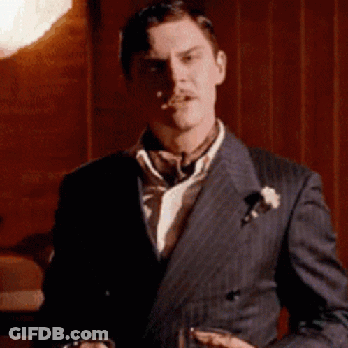 The Man Is Wearing A Suit And Tie And Holding A Glass Of Whiskey . GIF