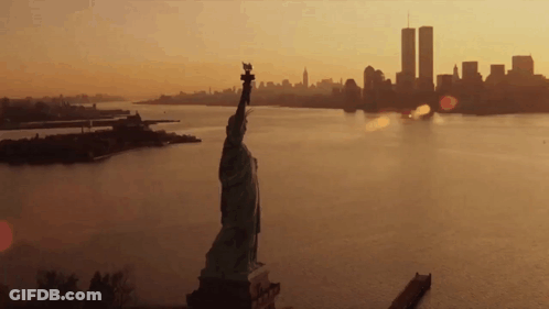 The Statue Of Liberty Is In The Foreground And The Twin Towers In The Background GIF
