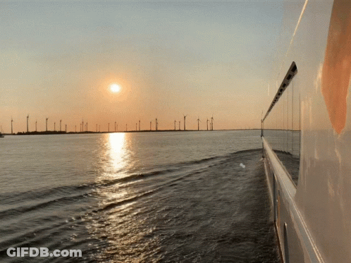 The Sun Is Setting Over A Body Of Water With Wind Turbines In The Background GIF
