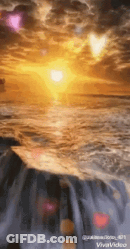 The Sun Is Setting Over The Ocean And A Waterfall Is In The Foreground . GIF