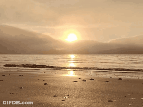 The Sun Is Setting Over The Ocean And Mountains In The Background GIF