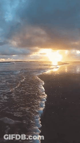 The Sun Is Setting Over The Ocean And The Waves Are Crashing On The Beach GIF