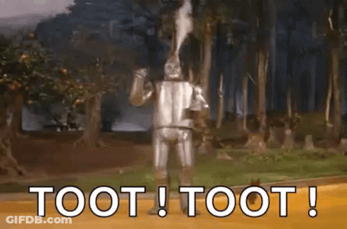The Tin Man From The Wizard Of Oz Is Blowing Smoke Out Of His Mouth While Standing On A Dirt Road . GIF