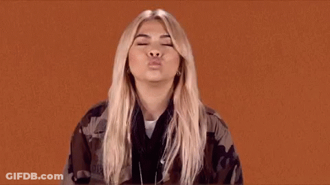 The Woman Is Wearing A Camouflage Jacket And Blowing A Kiss . GIF