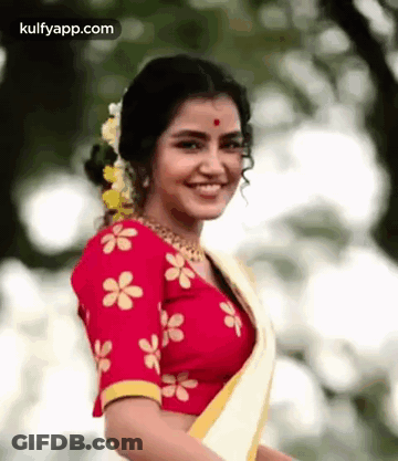The Woman Is Wearing A Red Blouse With Yellow Flowers On It And A White Saree . GIF