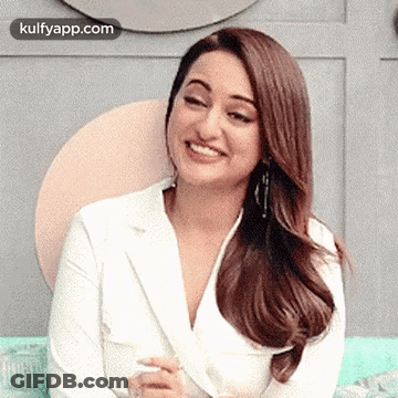 The Woman Is Wearing A White Jacket And Smiling While Sitting On A Couch . GIF