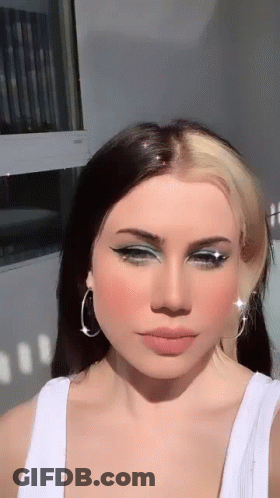 The Woman Is Wearing A White Tank Top And Earrings . GIF