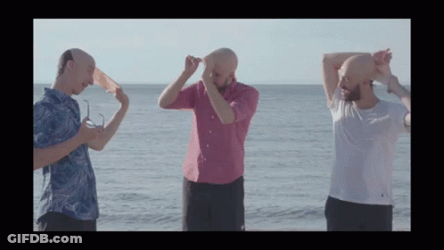 Three Bald Men Are Standing On The Beach With Their Heads In The Air GIF