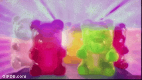 Three Colorful Gummy Bears Are Sitting Next To Each Other On A Pink Surface GIF